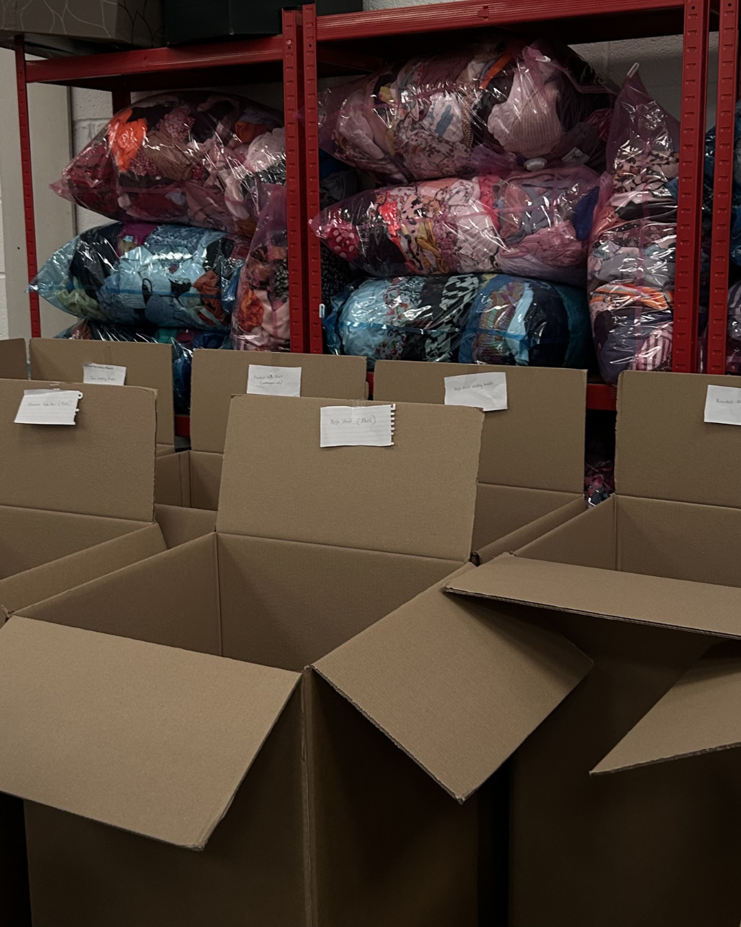 Cardboard boxes with labels in a warehouse setting with plastic-wrapped items on shelves.